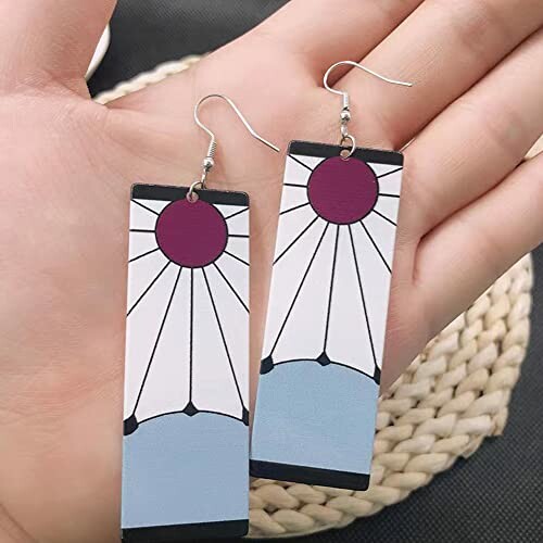 Hand holding geometric earrings with sunburst design.