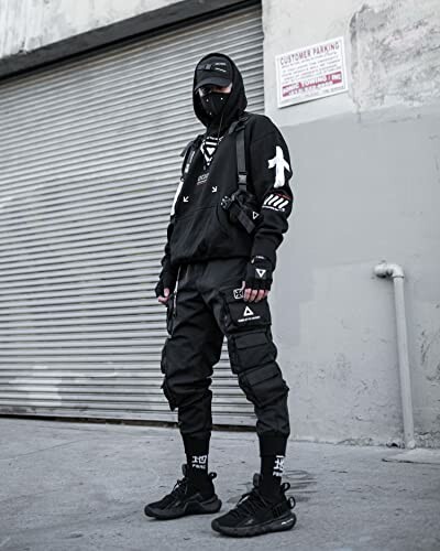 Person in black streetwear with mask and cap standing in front of a garage door.