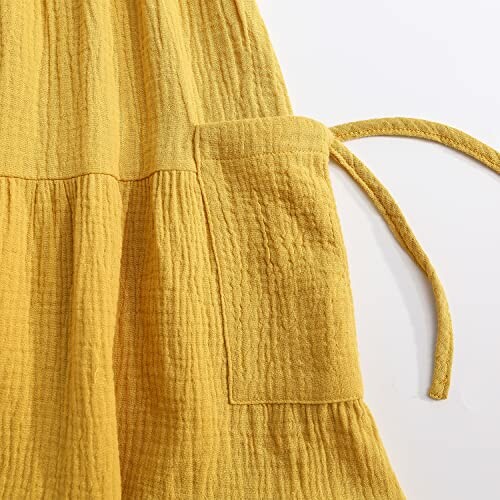 Close-up of a yellow textured fabric dress with a pocket and tied strap.